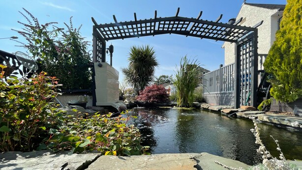 A stone bridge over a pond with surrounding greenery and a building in the background. - Bojangles Guest House (Gretna)