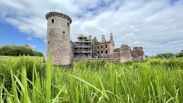 A historic castle with a prominent tower, surrounded by lush green grass and trees.
