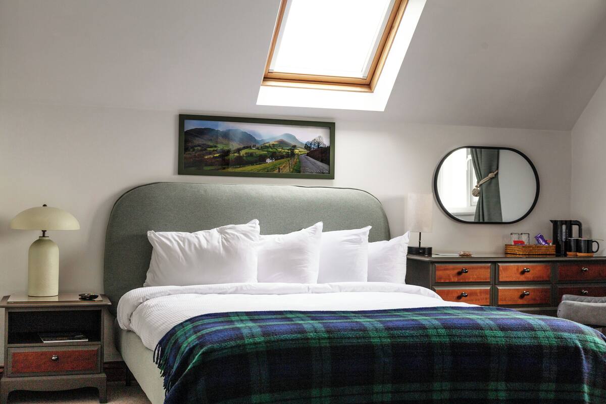 A bedroom with a bed, a nightstand, a dresser, a mirror, and a skylight.