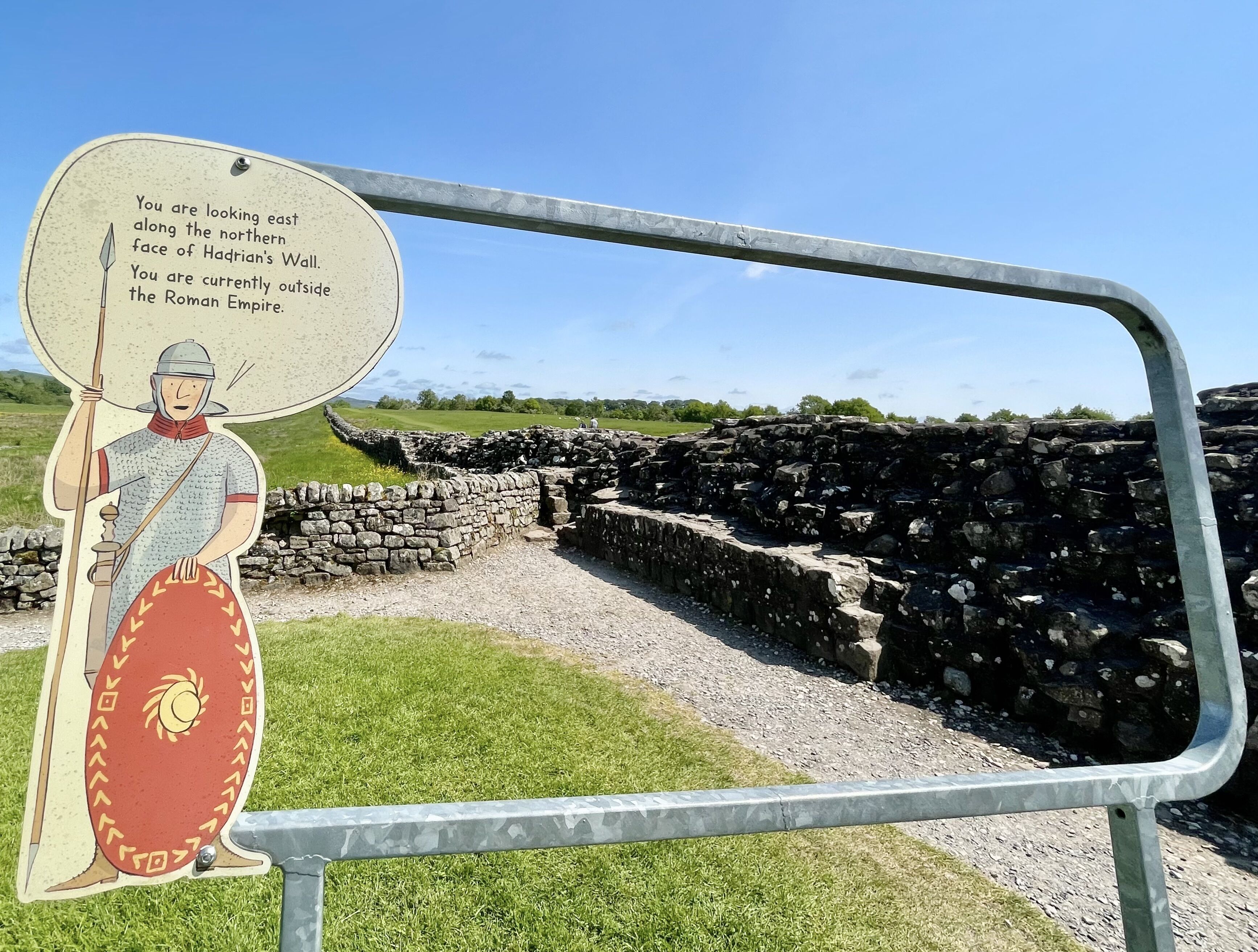A historical reenactment scene with a soldier figure and Hadrian's Wall ruins.