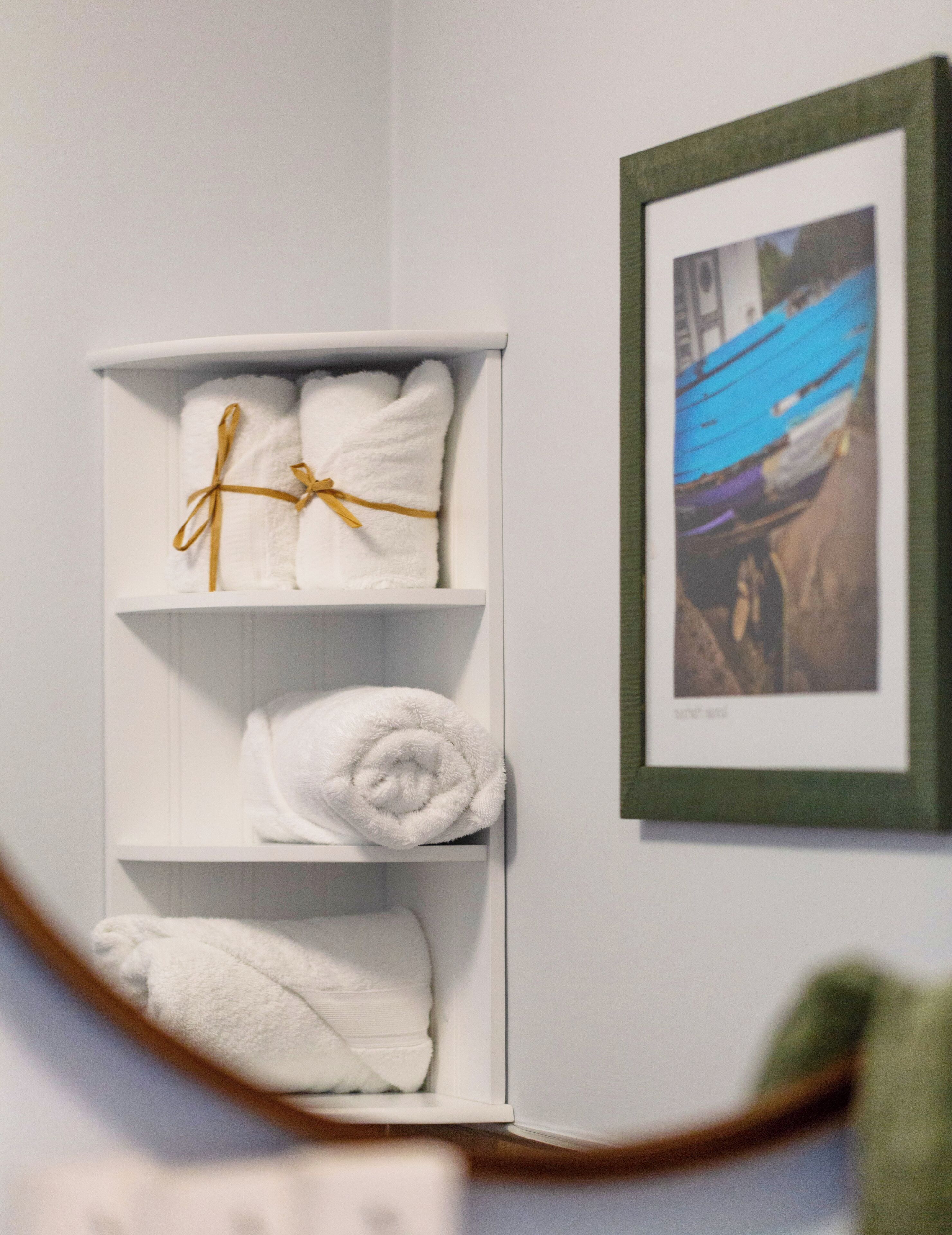 A white shelf with neatly folded white towels, some tied with a gold ribbon.