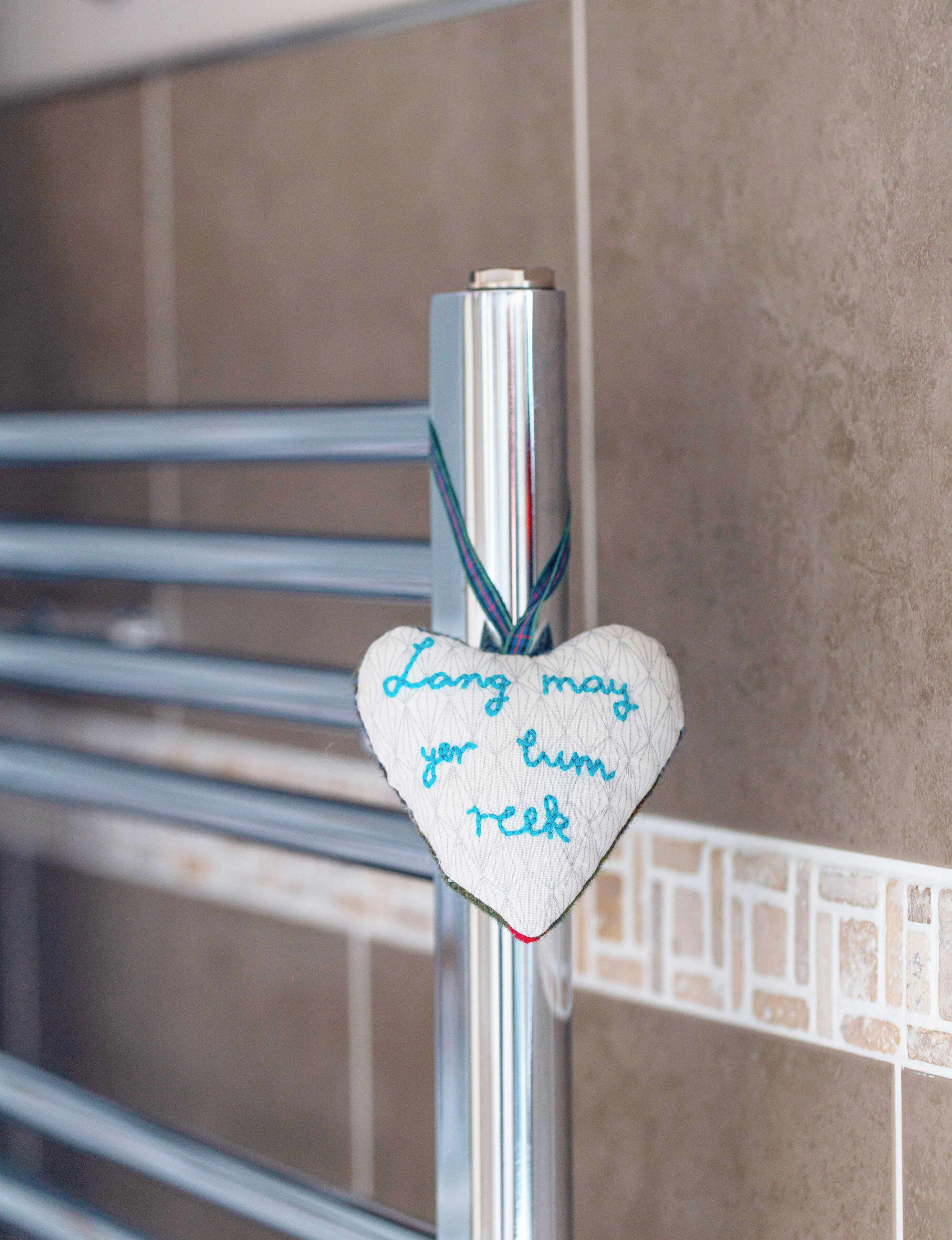 Een hartvormige decoratie met een berichtje bevestigd aan een metalen leuning in een badkamer.