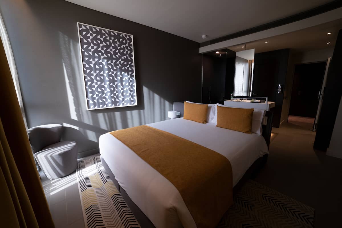 Una habitación de hotel moderna con una cama grande, zona de estar, baño y pasillo.