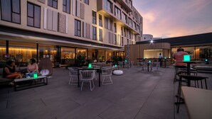 Een terras met tafels en stoelen, een gebouw met grote ramen en een bar.
