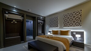 Een moderne hotelkamer met een groot bed, een bankje, een inloopkast en een douchecel.