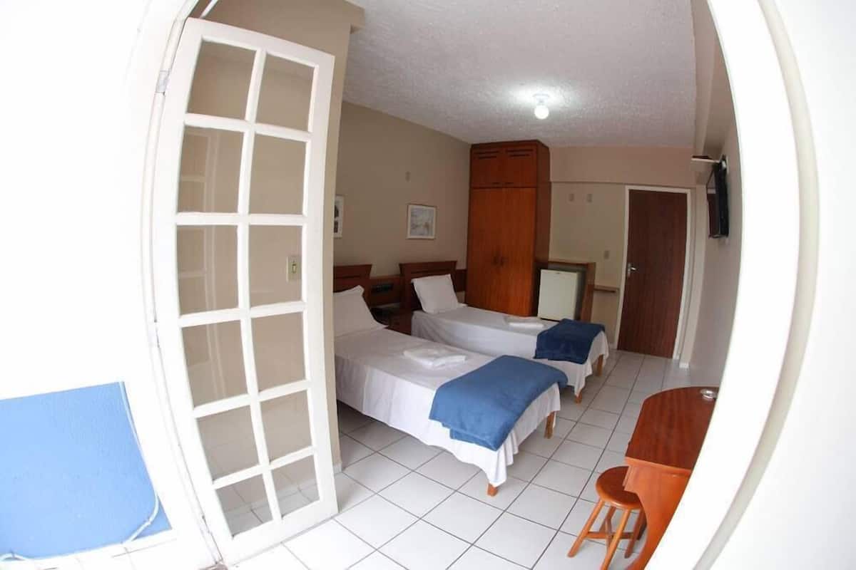 A room with two beds, a wooden wardrobe, a desk, and a chair.