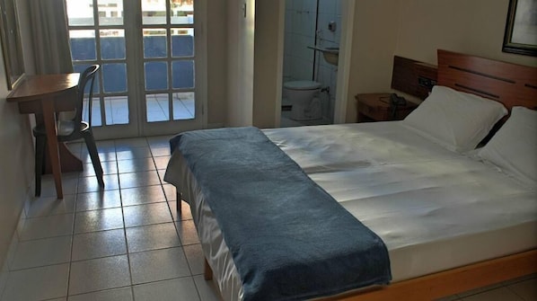 Habitación de hotel con cama, escritorio, silla y vistas al exterior a través de una ventana.