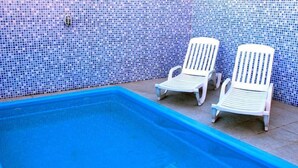 Una piscina con dos sillones blancos y un muro con azulejos.