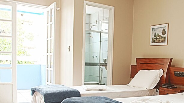 Habitación de hotel con dos camas, baño con ducha de vidrio y vista a zonas verdes.