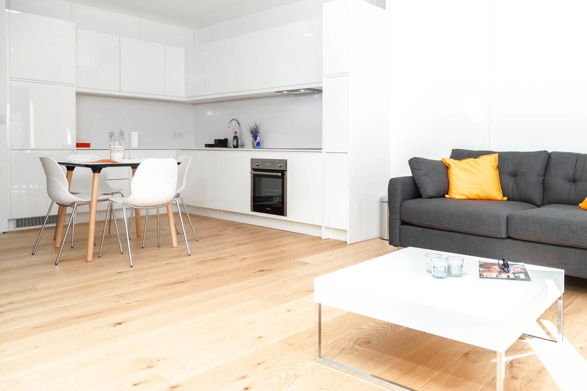 A modern living space with a grey sofa, white coffee table, and a dining area with chairs and a table.