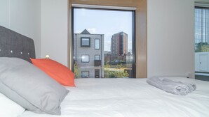 Moderni hotellihuone, jossa on suuri sänky, näkymä kaupungin rakennuksiin ja liukuovi parvekkeelle.