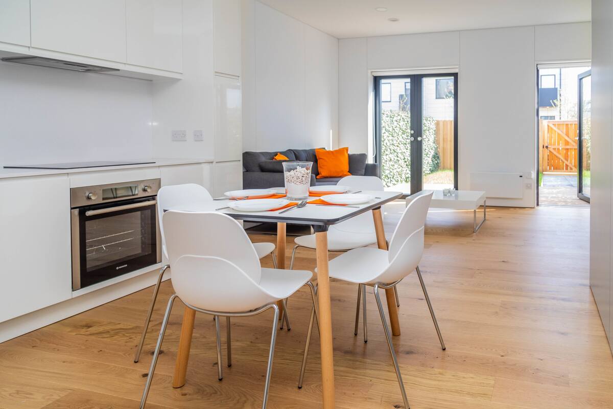 A modern kitchen with white cabinets, a built-in oven, and a dining area with a table, chairs, and a glass of milk.