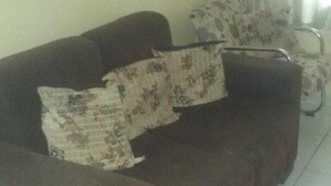 A living room with a brown sofa, patterned cushions, a painting on the wall, and a window with curtains. - Vila Mirante (Campina Grande)
