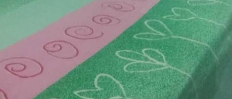 A bed with a green and pink bedspread, a red heart-shaped pillow, and a green and pink striped pillow.