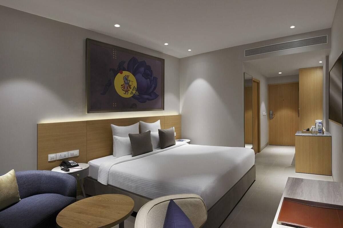 A hotel room with a bed, bedside table, lamp, and a painting on the wall.