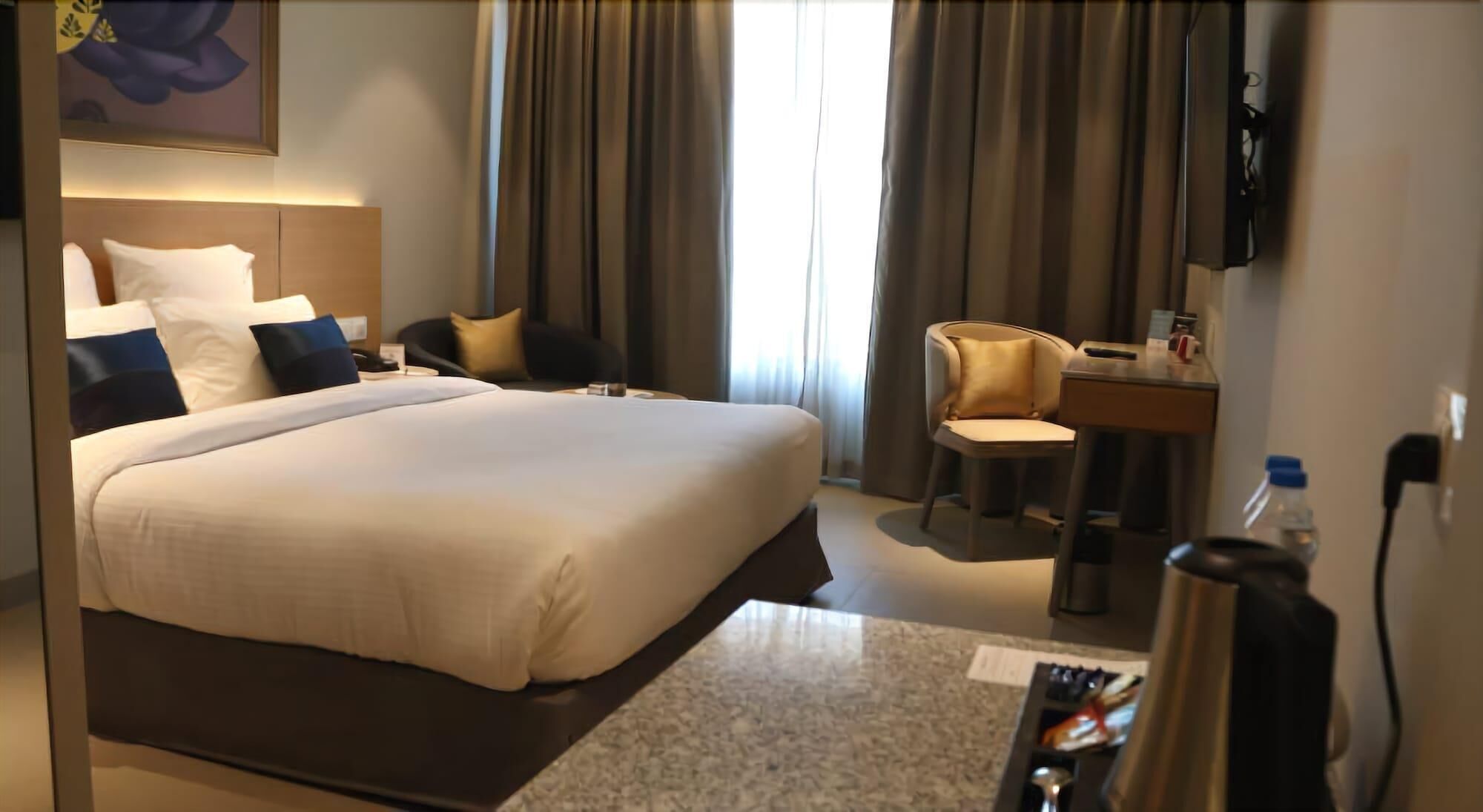 A hotel room with a large bed, a desk, a chair, a TV, and a water bottle.