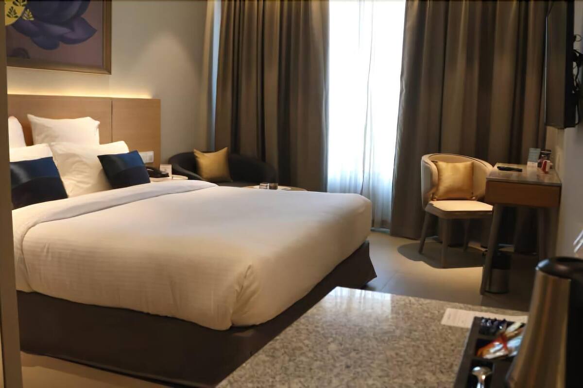 A hotel room with a large bed, a desk, a chair, a TV, and a water bottle.