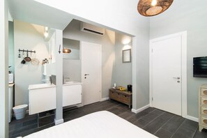 A modern bathroom with a white sink, mirror, and a vanity cabinet. There is a door leading to another room and a television mounted on the wall. - Talnet Apartment (Tel Aviv)