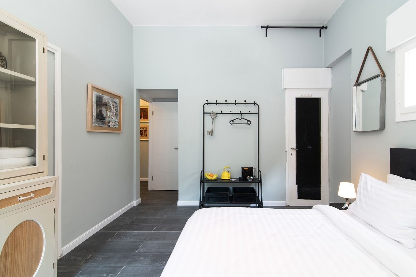 A hotel room with a bed, a wardrobe, a coat rack with keys, and a door leading to a hallway.