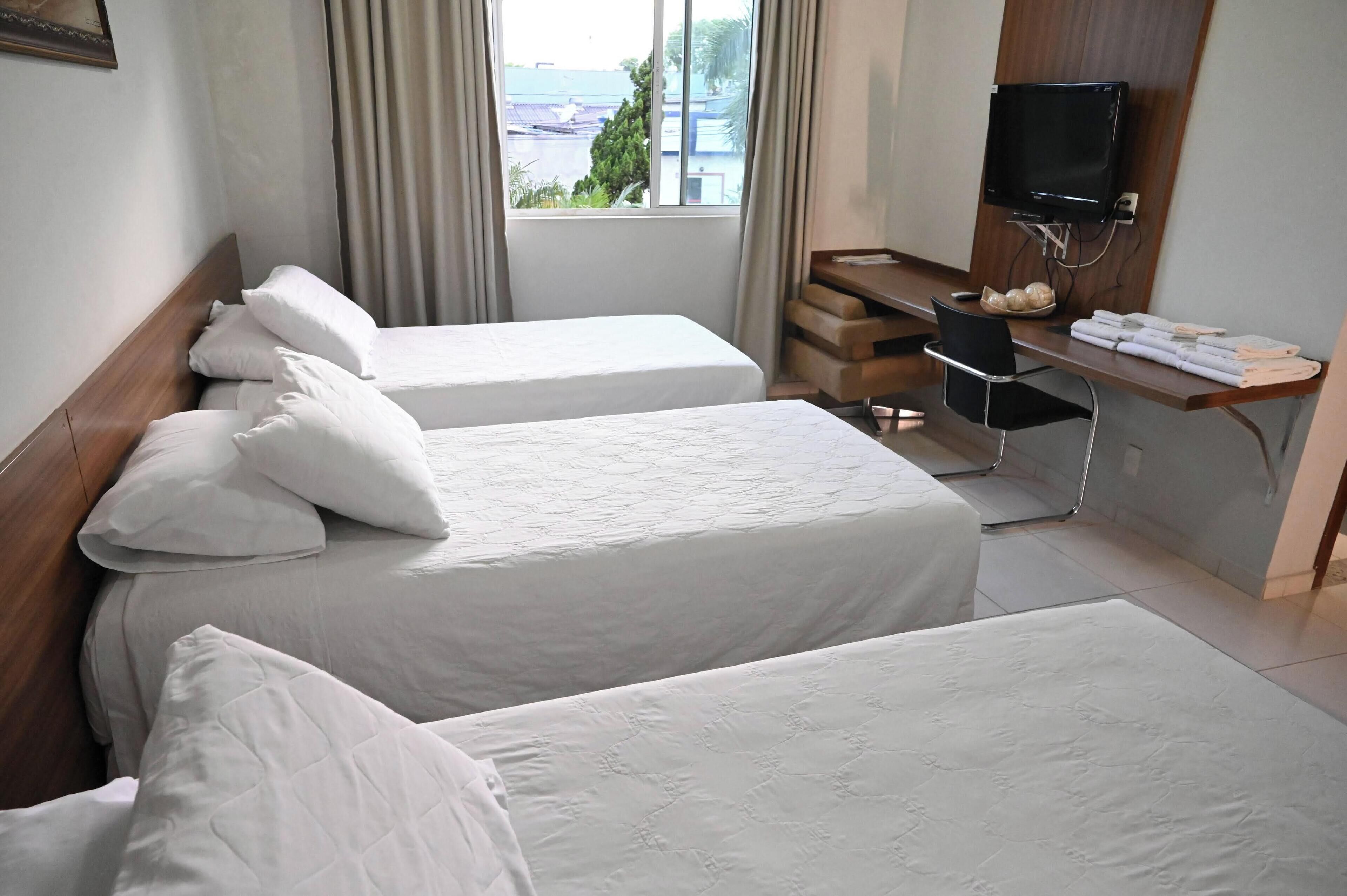 A hotel room with two beds, a desk with a computer, a TV, and a view of the city.