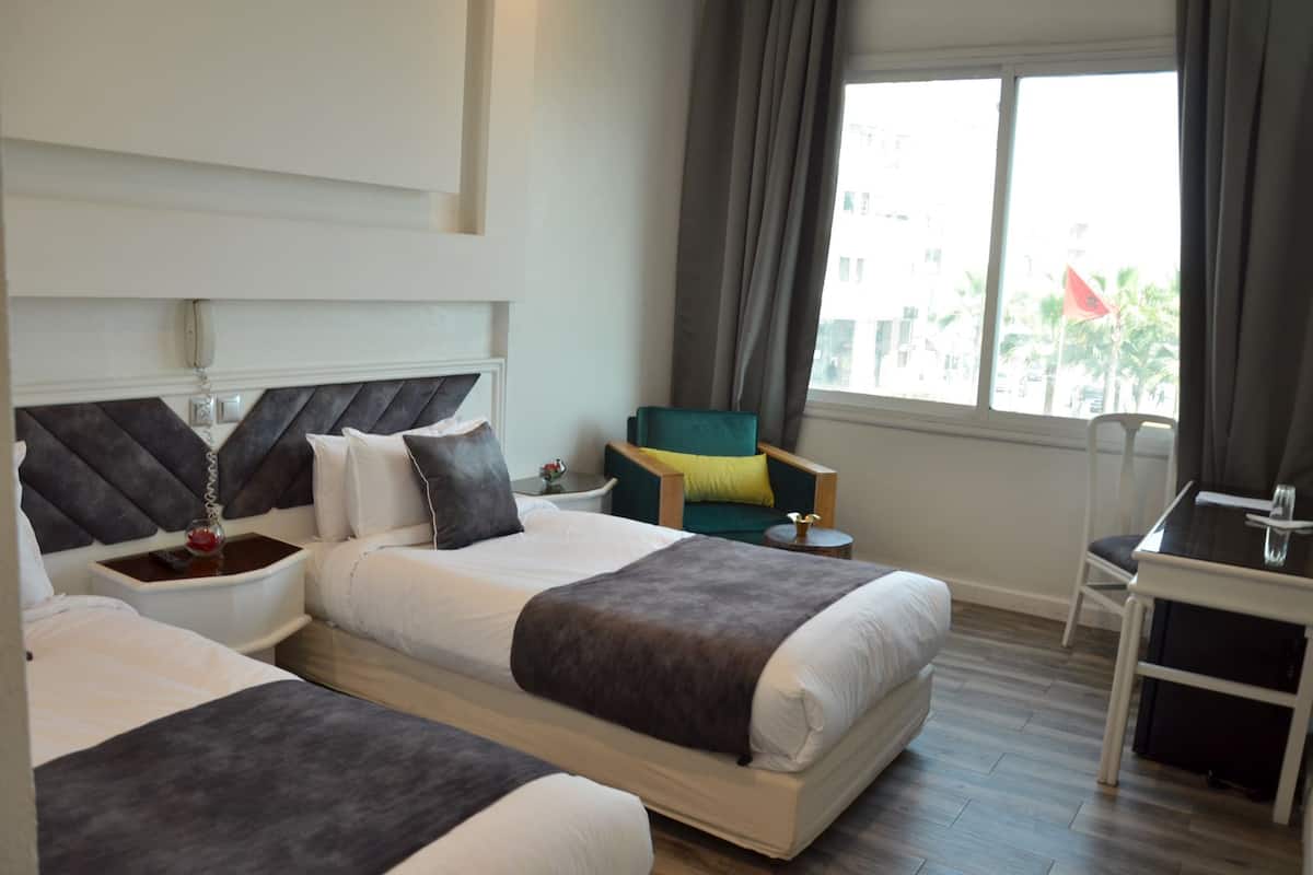 Una habitación de hotel con dos camas, un escritorio, una silla y un ventanal con cortinas.