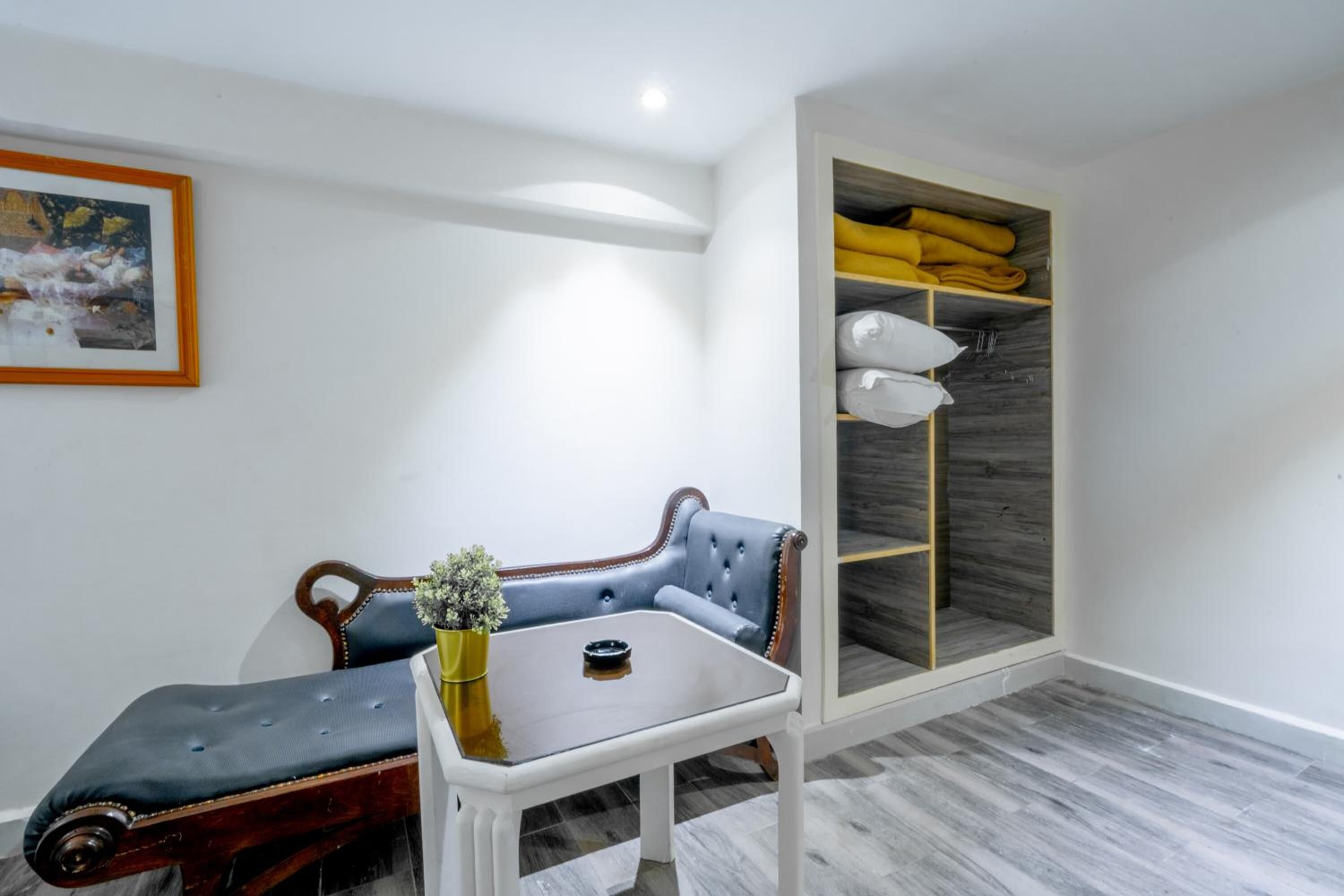 A room with a blue upholstered sofa, a small white table with a vase, and a wooden wardrobe with shelves.