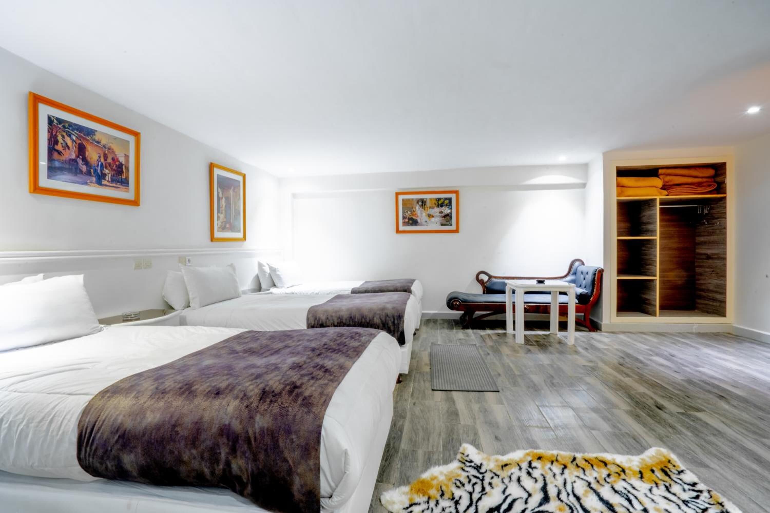 A hotel room with two beds, a desk, a chair, a wardrobe, and artwork on the walls.