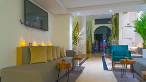 A modern living room with a sofa, two side tables, a teal armchair, and a flat-screen TV mounted on the wall.