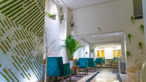 A lobby with teal chairs, a large plant, and a wall with green plants arranged in a pattern.