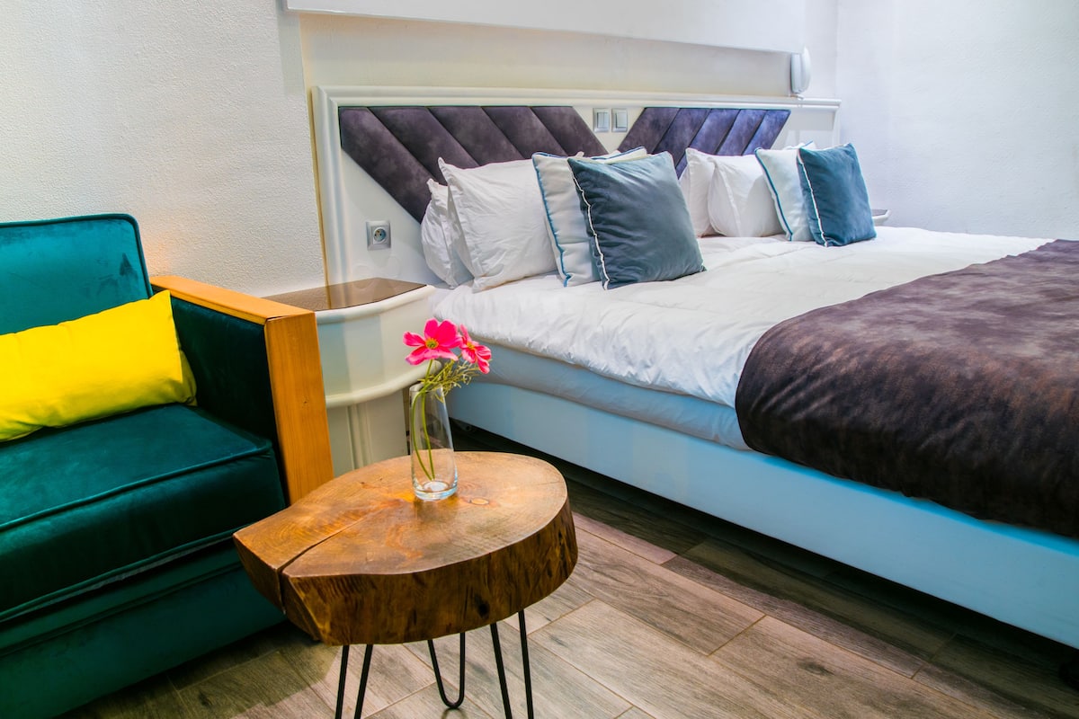 Una habitación de hotel moderna con una cama, un sofá verde y una pequeña mesa de madera con un jarrón de flores.