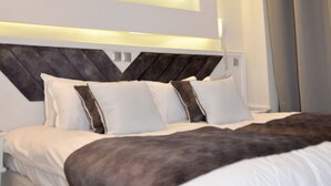 A modern bedroom with a large bed, geometric ceiling design, and a neutral color scheme.