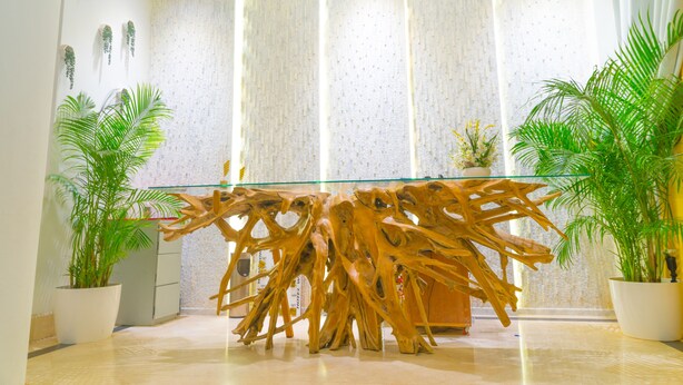 A reception area with a glass-top desk, wooden decor, potted plants, and a patterned wall.