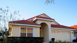 A single-story house with a red-tiled roof, a beige facade, and a garage with decorative awnings. - 5 Br Pool Home with Spa in Aviana (Davenport)