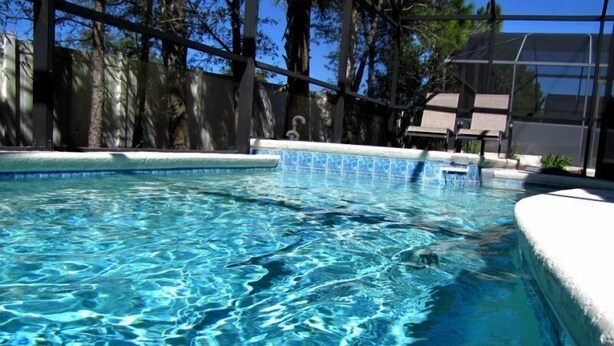 A clear swimming pool with a tiled edge, surrounded by trees and a building in the background. - 5 Br Pool Home with Spa in Aviana (Davenport)