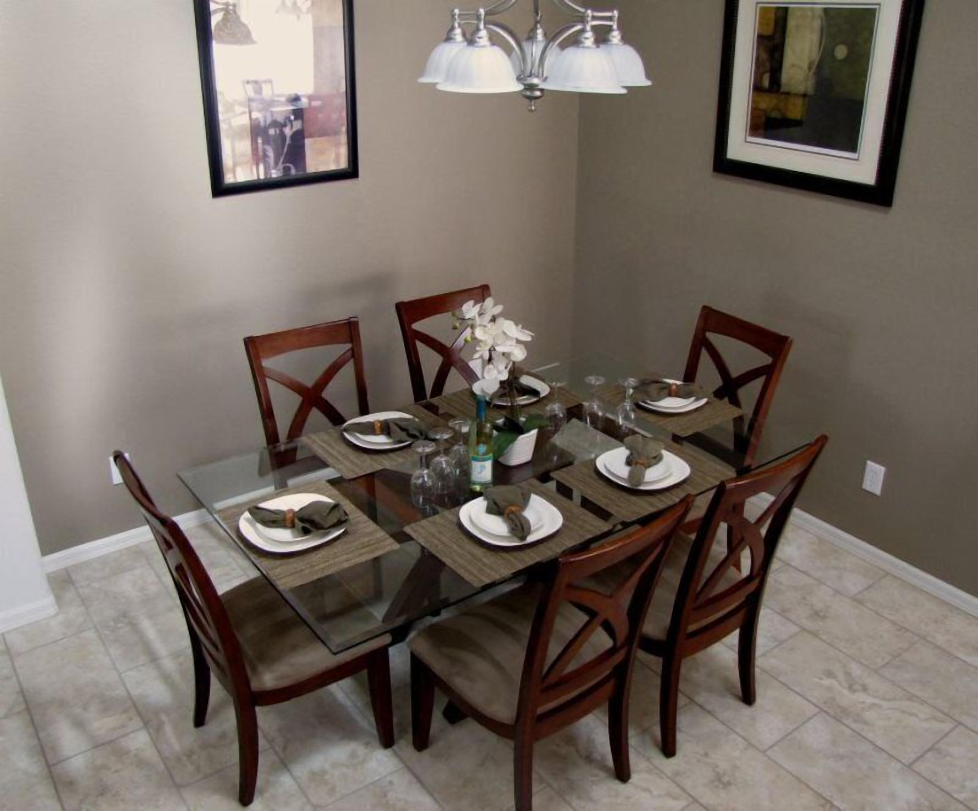 A dining area with a glass table surrounded by wooden chairs, a vase with flowers, and a chandelier.