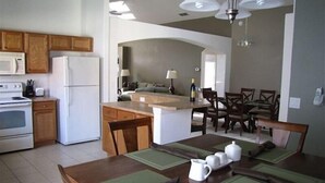 A modern kitchen with wooden cabinets, a built-in oven, and a refrigerator. There is a dining area with a table set for four, green placemats, and a pitcher of water. - 5 Br Pool Home with Spa in Aviana (Davenport)