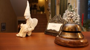 A wooden reception desk with a white ceramic figure, a brass bell, and a framed sign. - Conviva Hotel (Panevezys)