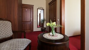 A room with a wooden chair, a round table with a vase of flowers, and a mirror on the wall. - Conviva Hotel (Panevezys)