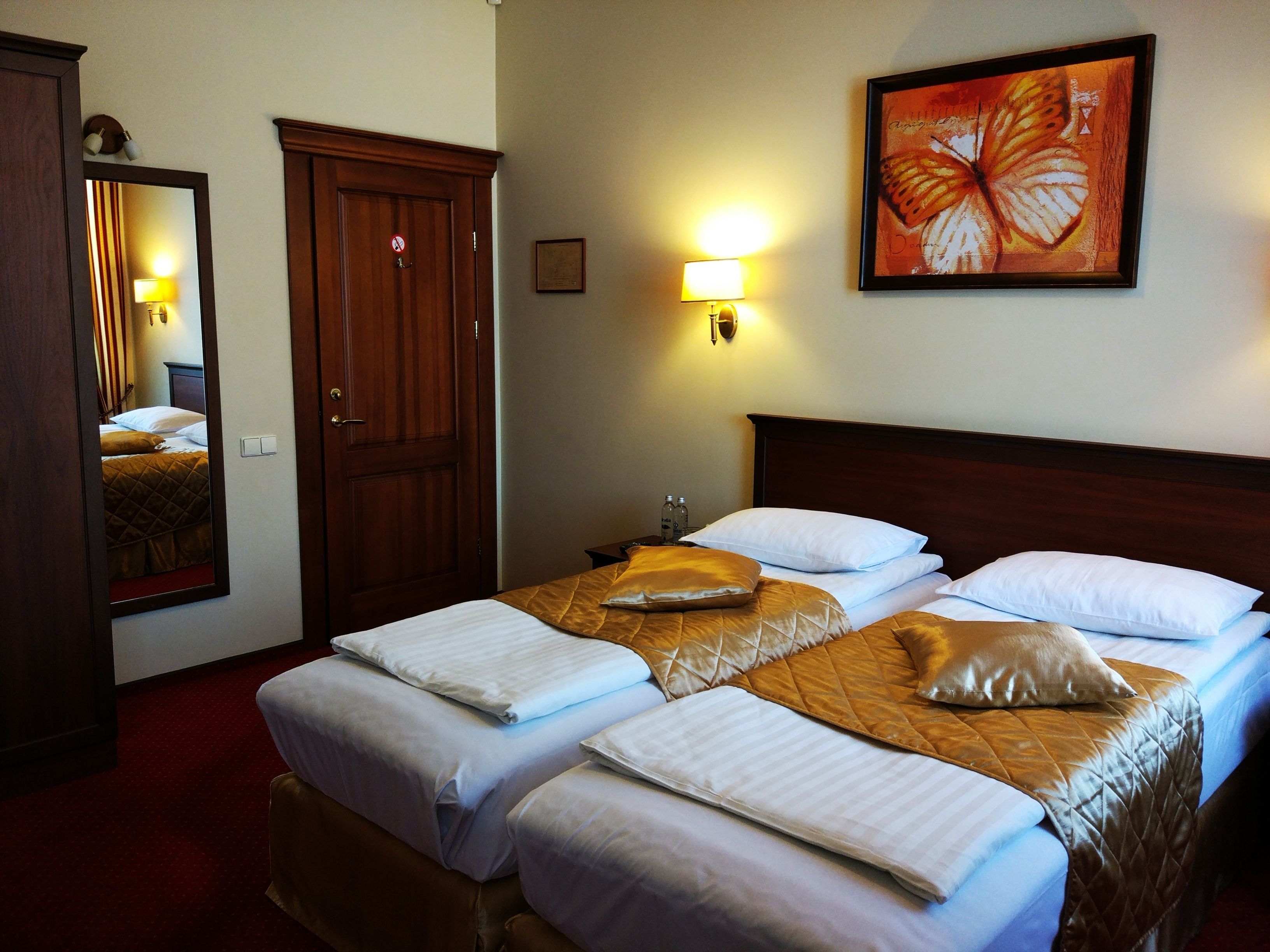 A hotel room with a large bed, two bedside tables, a mirror, a wall-mounted light, and a framed artwork.