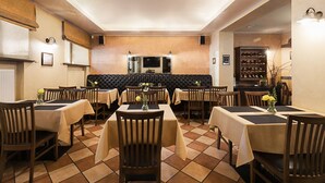 A restaurant with multiple tables and chairs, a black cushioned booth area, and a wine rack in the background. - Conviva Hotel (Panevezys)