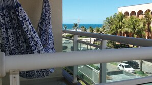 A balcony with a view of a beach, palm trees, and a building with arches.