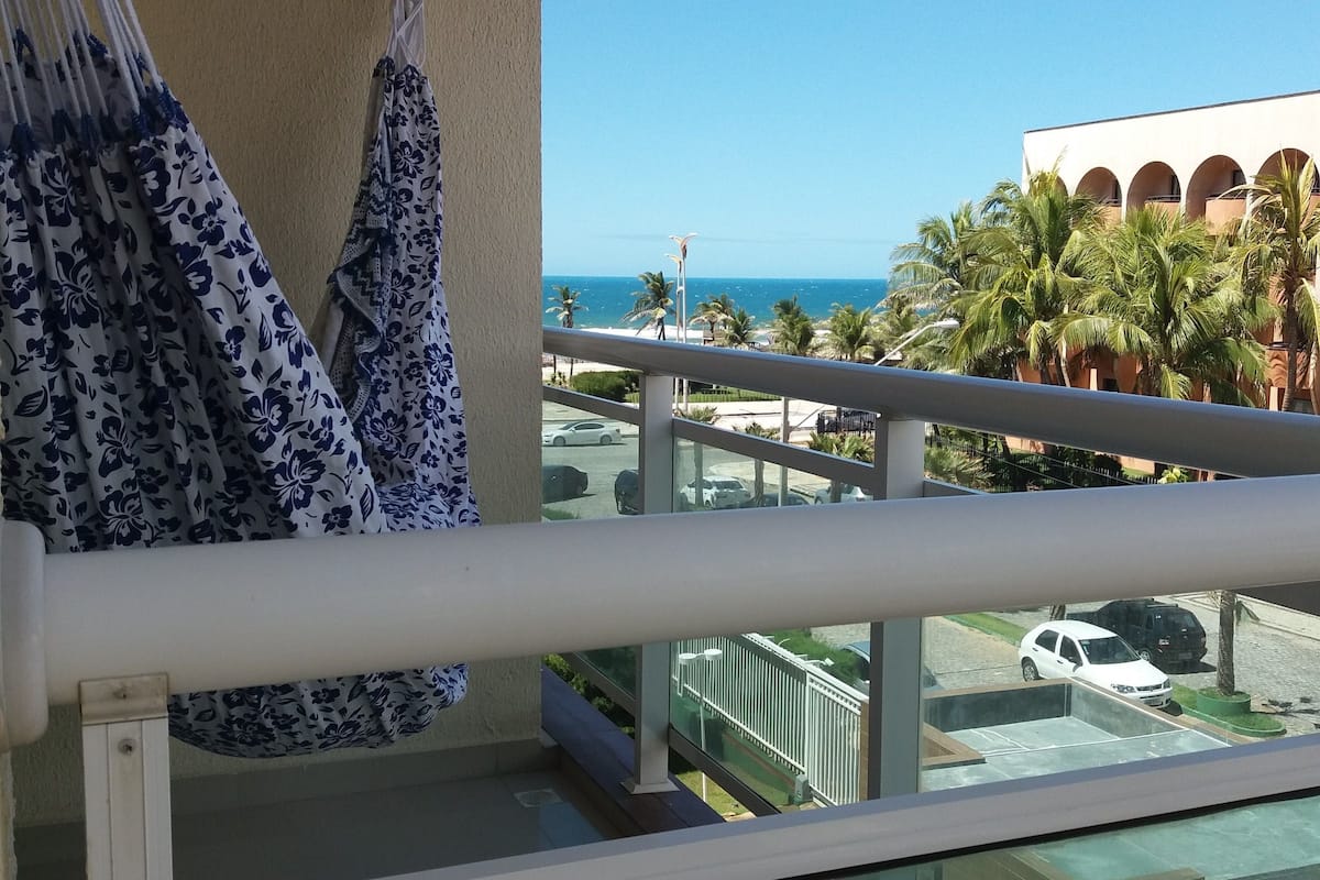 Ein Balkon mit Blick auf einen Strand, Palmen und ein Gebäude mit Bögen.