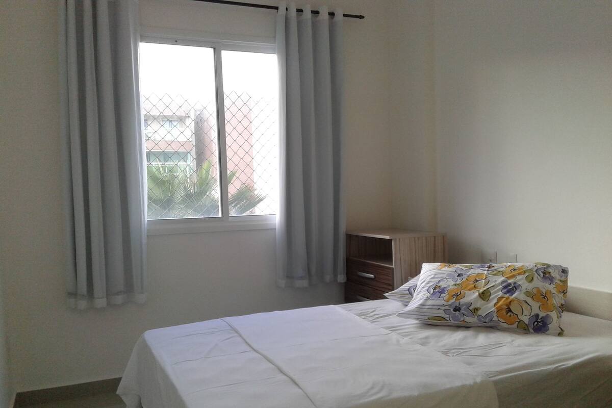 Ein Schlafzimmer mit Bett, einem Fenster mit Vorhängen und einem kleinen Nachttisch.