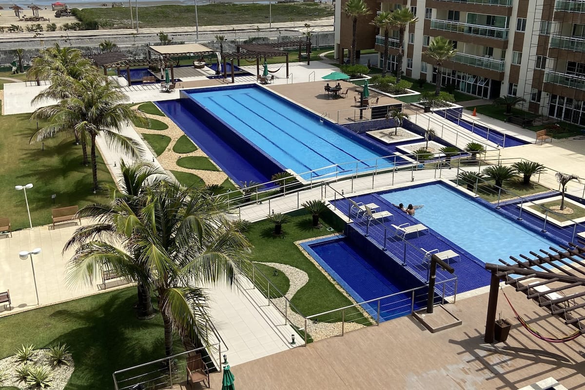 Ein Hotel mit mehreren Schwimmbecken, Meerblick und einem Parkplatz.