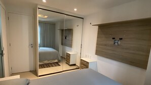 A modern hotel room with a large bed, a walk-in closet, a mirror, and a wooden headboard.