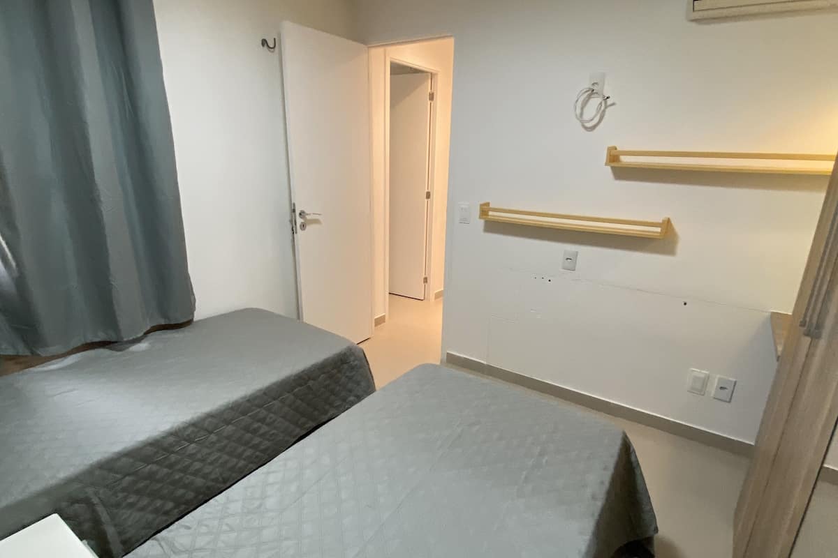 Ein Zimmer mit zwei Betten, einer Tür, einer Wand-Klimaanlage und einer Leuchte.