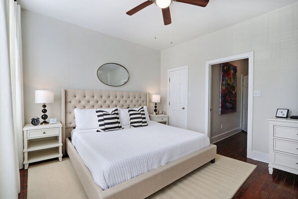A bedroom with a large bed, two bedside tables, a ceiling fan, and a door leading to another room. - Gallery Stays - Amiri Pop (Savannah)