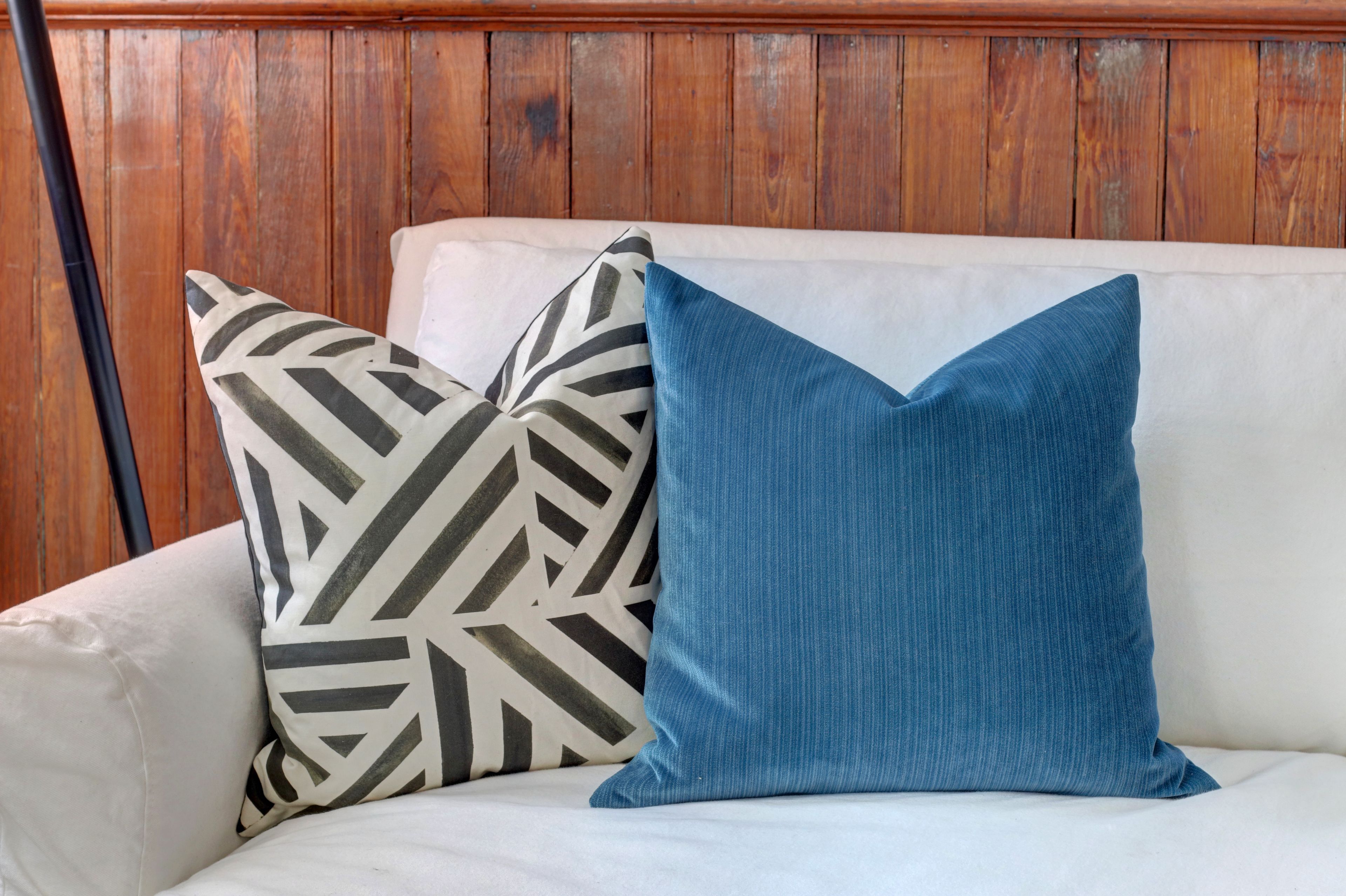 A white sofa with two pillows, one with a geometric pattern and the other solid blue.