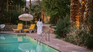 A poolside area with lounge chairs, a pool, and a person in a white robe.