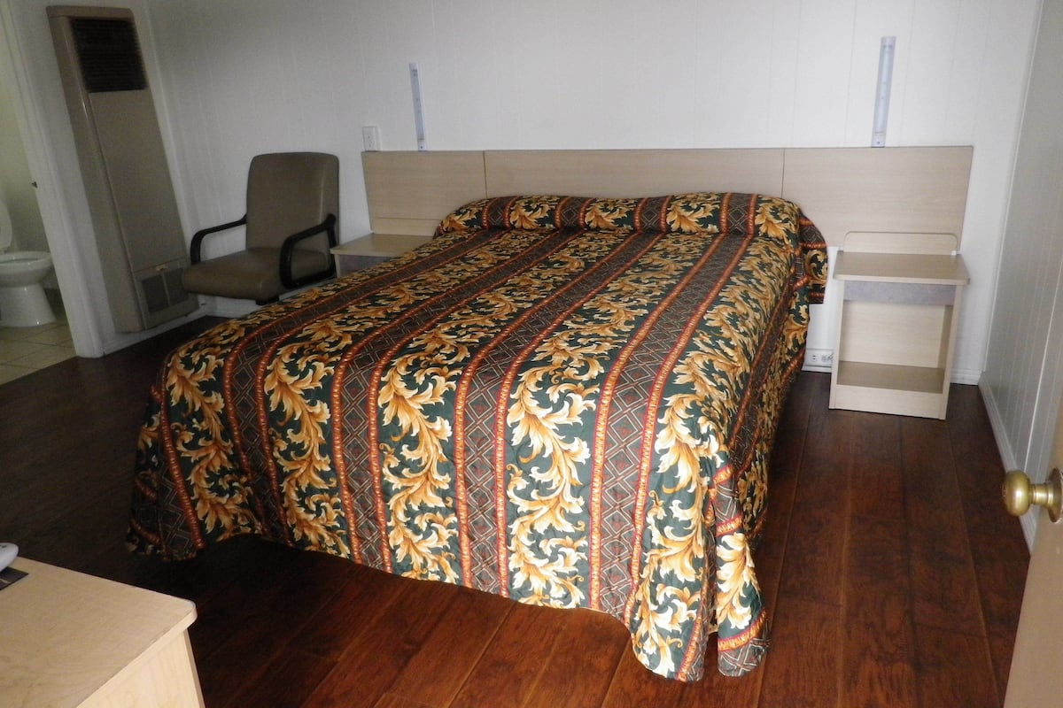 A bedroom with a bed, a chair, a bedside table, and a door.